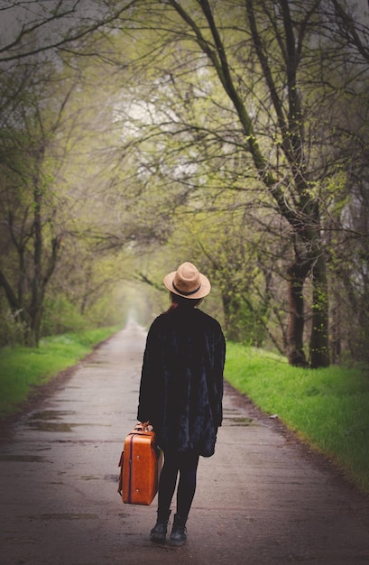 L'arrière de la jeune fille avec une valise au printemps allée à la campagne