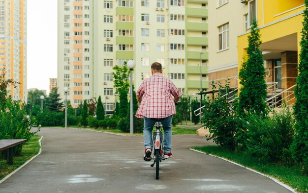 L'arrière d'un jeune homme marche sur un vélo de ville le soir dans la cour Un homme adulte en vêtements décontractés fait du vélo dans la cour Eco transport