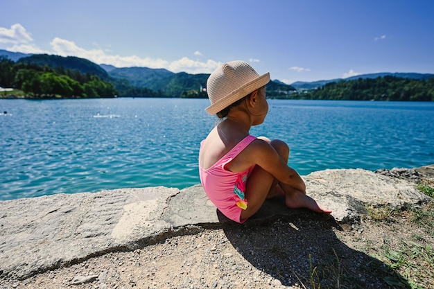 L'arrière de la petite fille est un maillot de bain et un chapeau assis dans la jetée de la belle vue sur le lac de Bled en Slovénie