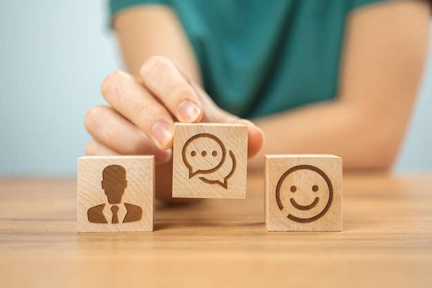Arrière-plan du concept de service du centre client Aider et soutenir la coopération Cubes en bois avec des icônes de sourire et une jeune femme main dans la photo de bureau