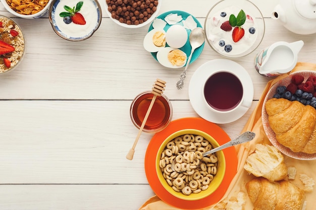 Arrière-plan Du Menu Du Petit-déjeuner Riche. Croissants Croustillants Français, Muesli, Yaourt, Café, Baies, Miel Et œufs Durs Pour De Savoureux Repas Du Matin Sur Table En Bois, Vue De Dessus, Espace De Copie