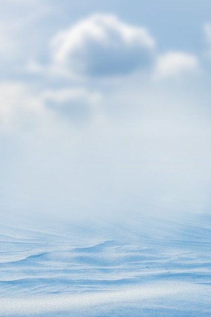 Arrière-plan enneigé, surface enneigée de la terre après un blizzard le matin au soleil avec des couches distinctes de neige et de ciel avec des nuages flous. Fond de Noël d'hiver