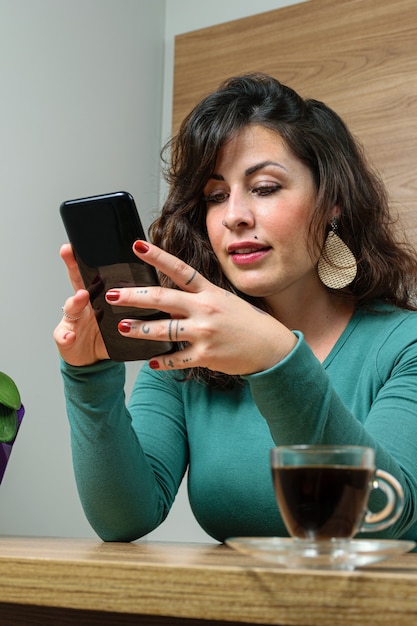 En arrière-plan, une femme brésilienne interagit avec son smartphone. En premier plan défocalisé, tasse de café.
