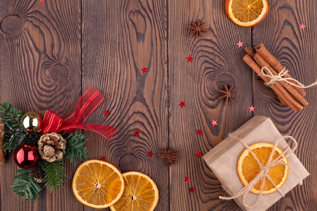 Arrière-plan festif de Noël avec un sapin de Noël décoré de perles de pomme de pin et de cadeaux emballés dans du papier kraft oranges séchées sur un fond en bois espace de copie à plat