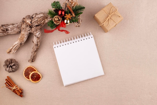 Arrière-plan de fête de Noël avec journal et sapin décoré de tiges de cannelle de cône de pin et cadeau enveloppé dans du papier kraft oranges séchées sur fond de tissu de lin espace de copie plat