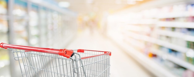 Arrière-plan flou flou d'allée de supermarché avec panier rouge vide