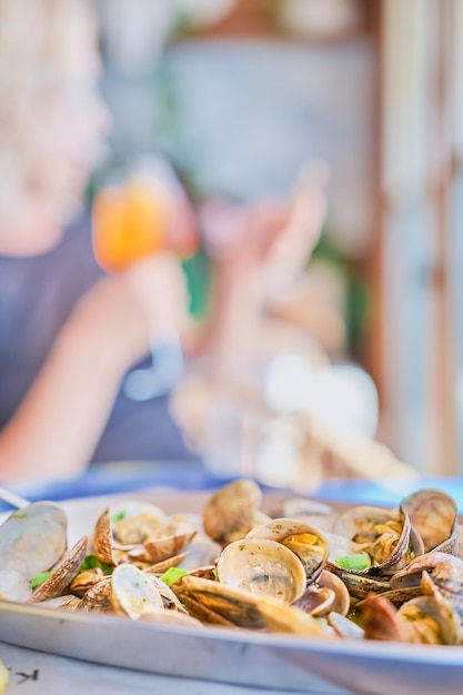 Arrière-plan flou avec un plat de palourdes vongole bouillies sur une table dans un cadre vertical de café en arrière-plan la silhouette d'une femme avec un verre de vin Idée pour un économiseur d'écran ou une bannière