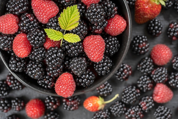 Arrière-plan de mûres et de framboises biologiques fraîches, gros plan. Beaucoup de baies crues de fruits sauvages juteux mûrs dans une assiette noire. Vue de dessus mûre et framboise