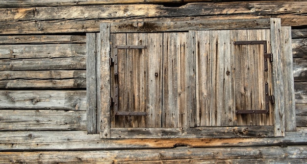 Arrière-plan et texture du bois d'un mur d'une vieille maison en bois avec des fenêtres fermées par des volets