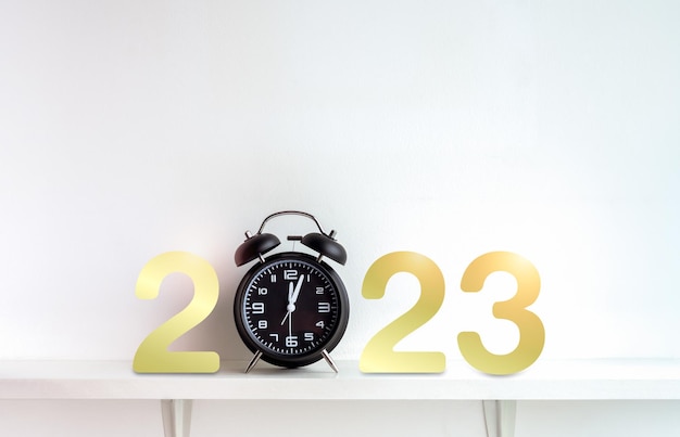 Arrière-plans de bonne année 2023 Numéros de calendrier dorés 2023 avec réveil noir après minuit sur étagère sur fond blanc avec espace de copie Concept de joyeux Noël et bonne année