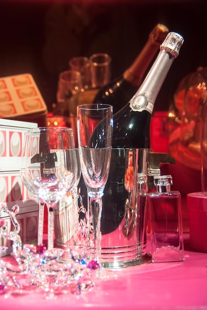 Arrière-plans luxueux avec une bouteille de champagne rafraîchissante et des figurines en cristal de verre flacons de parfum coffrets cadeaux et nappe rose