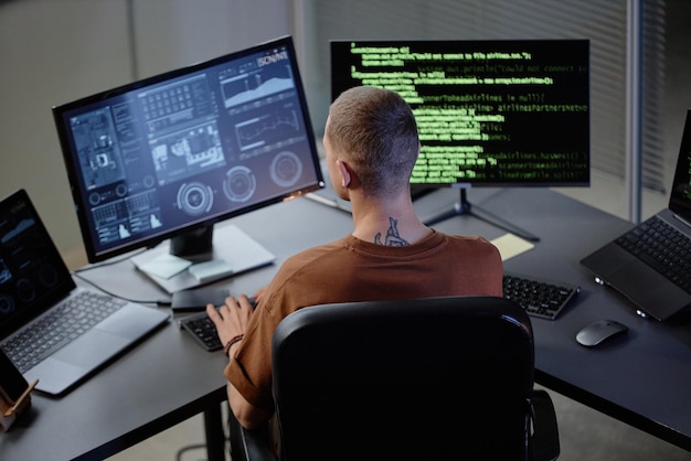 Arrière d'un programmeur d'ordinateur masculin travaillant à son bureau en regardant des écrans avec du code dans son bureau