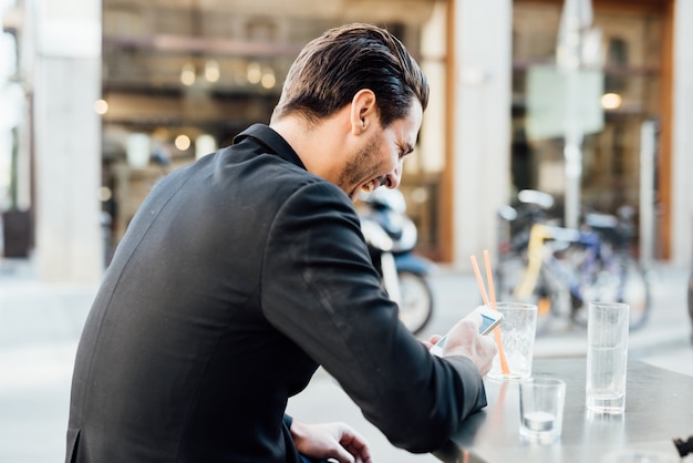 Arrière, vue, de, jeune, beau, homme, assis, sur, a, barre, dans, les, centre ville, utilisation, a, smartphone