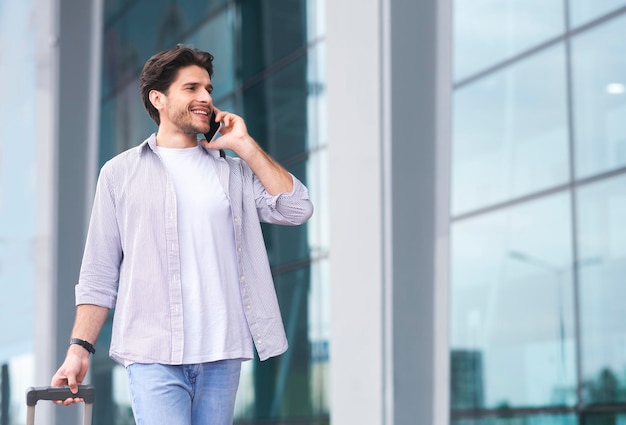 En arrivant à l'aéroport, un homme parle sur un téléphone portable et marche avec des bagages