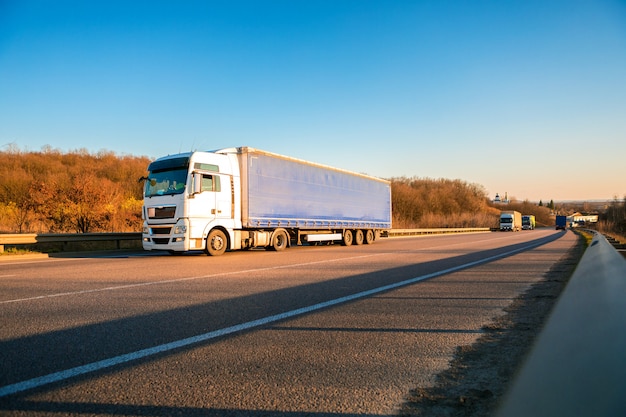 Arrivée d&#39;un camion blanc sur la route dans un paysage rural au coucher du soleil