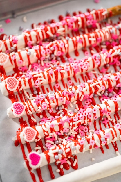 Arroser de chocolat fondu sur des tiges de bretzels trempées dans le chocolat et décorer avec des pépites pour faire des tiges de bretzels recouvertes de chocolat pour la Saint-Valentin