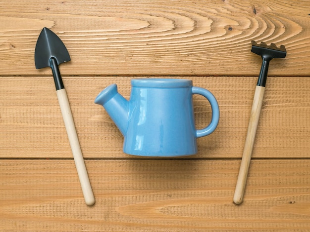 Arrosoir bleu entre une pelle et un râteau sur un fond en bois Un ensemble d'outils de jardin