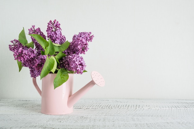 Arrosoir rose décoratif avec des fleurs lilas violettes sur une table en bois blanc. Concept de jardinage. Printemps et été.