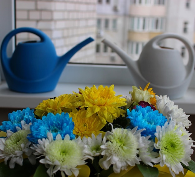 Arrosoirs en plastique blanc et bleu sur un rebord de fenêtre avec FLovers en premier plan