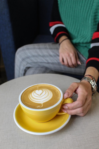 Photo art café chaud dans une tasse jaune dans la main d'une belle femme