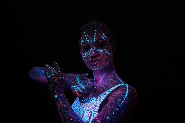 Art femme cosmos en lumière ultraviolette. Le corps entier est couvert de gouttelettes colorées. Fille posant dans le noir. Bruit, flou