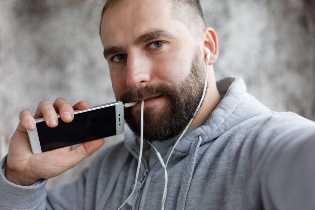 Art, personnes, émotions, musique, 4K et concept de style de vie - Un modèle sorti en studio met des écouteurs sur les roches, de l'électronique en musique. Le jeune bel homme barbu écoute le smartphone de musique dans des écouteurs