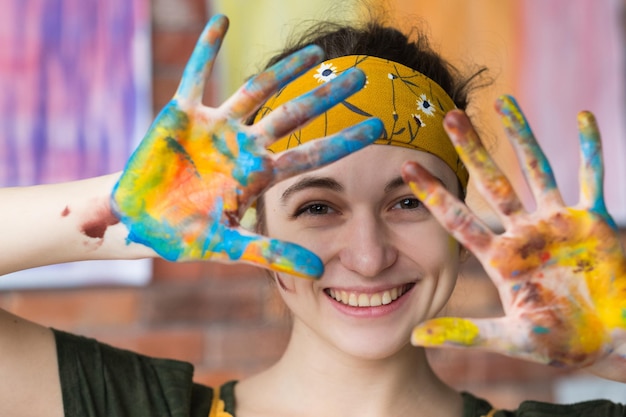 Art-thérapie Portrait en gros plan d'une jeune artiste féminine s'amusant en studio souriant montrant les mains sales avec de la peinture