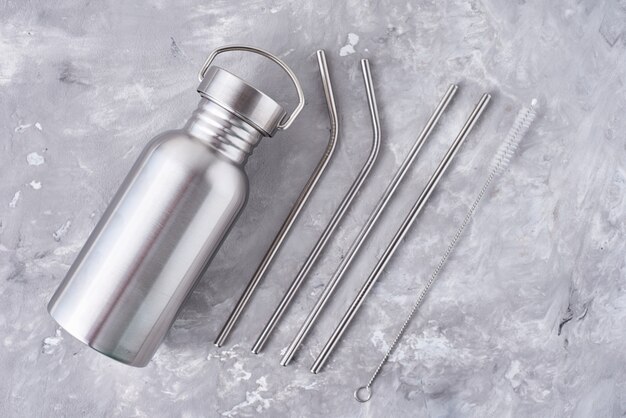 Articles réutilisables sans plastique sur une surface grise. Vue de dessus de la bouteille d'aluminium et des tubes métalliques. Concept écologique zéro déchet