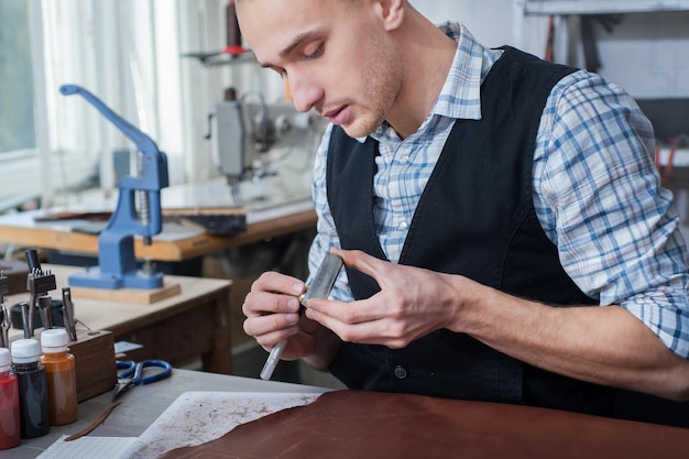 Un artisan aiguise le bord d'un outil en cuir dans un atelier