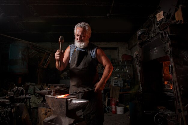 Artisan forgeron en tablier travaille dans la boutique du forgeron