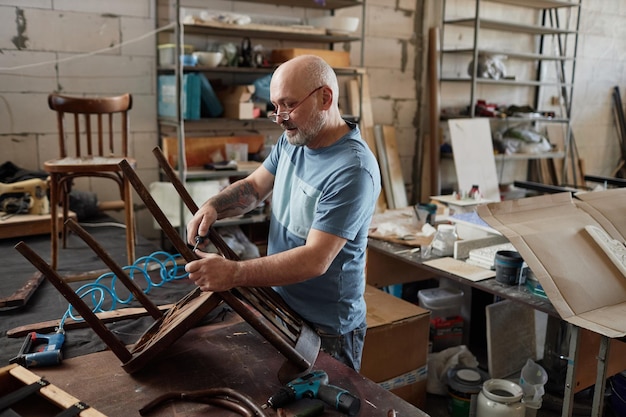 Artisan senior restaurant une chaise dans un atelier de meubles