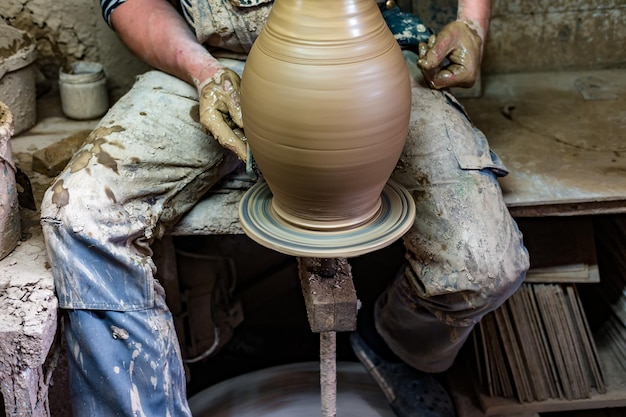 Artisan en vêtements sales moulant l'argile dans la forme souhaitée sur le tour du potier