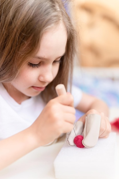 Artisanat en feutre de laine fait à la main avec une aiguille petite fille artisan de neuf ans avec la main fait un jouet créatif fait de poils de mouton personnes enfants passe-temps et activité de feutrage artisanal