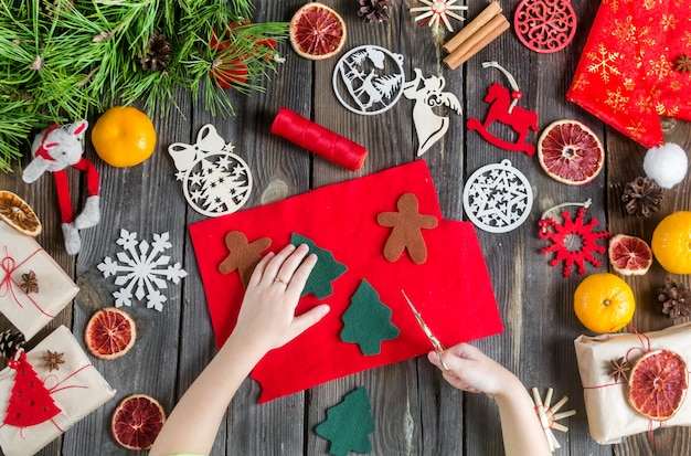 Artisanat de Noël Fille coupe des jouets de ciseaux en feutre naturel sur la table à côté des décorations de vacances