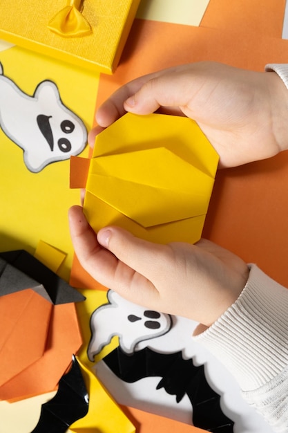 Artisanat d'origami pour citrouille d'Halloween en papier entre les mains d'un enfant vue de dessus