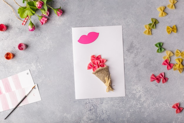 Artisanat en papier pour la fête des mères, le 8 mars ou l'anniversaire. Petit enfant fait un bouquet de fleurs en papier coloré et pâtes colorées.