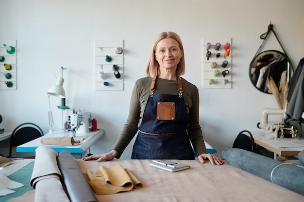 Artisane mature souriante en tablier regardant la caméra en atelier