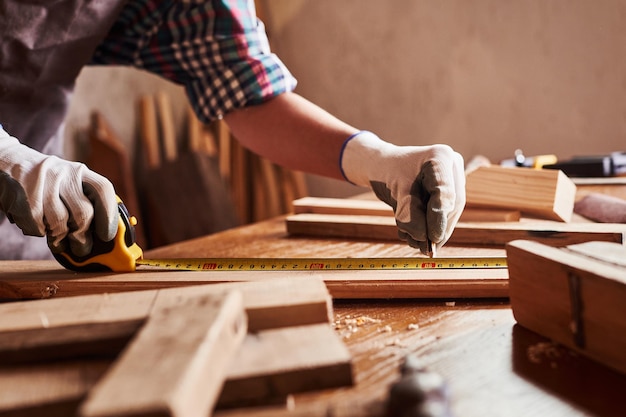 Les artisans féminins utilisent un ruban à mesurer pour assembler des pièces en bois Ouvrier du bâtiment tenir la règle Charpentier professionnel au travail mesurant des planches de bois