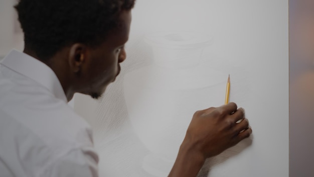 Artiste afro-américain créant un dessin de vase avec un crayon sur une toile blanche au studio d'art. Jeune adulte noir utilisant des outils et instruments d'artisanat pour un projet innovant de chef-d'œuvre moderne