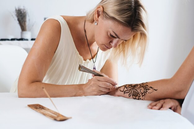 Artiste appliquant un tatouage floral au henné sur les mains des femmes pour la beauté