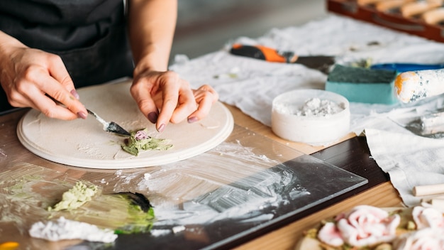 Artiste au travail. Lieu de travail de studio. Oeuvre en céramique en cours. Artisanat. Femme avec des outils de modélisation en main.