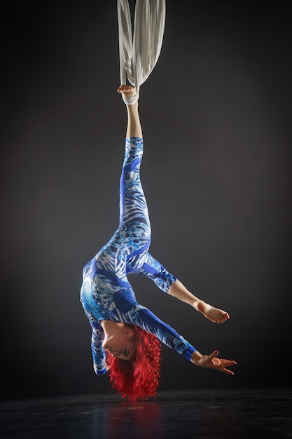 Photo artiste de cirque aérien sexy athlétique avec rousse en costume bleu faisant des tours sur la soie aérienne.