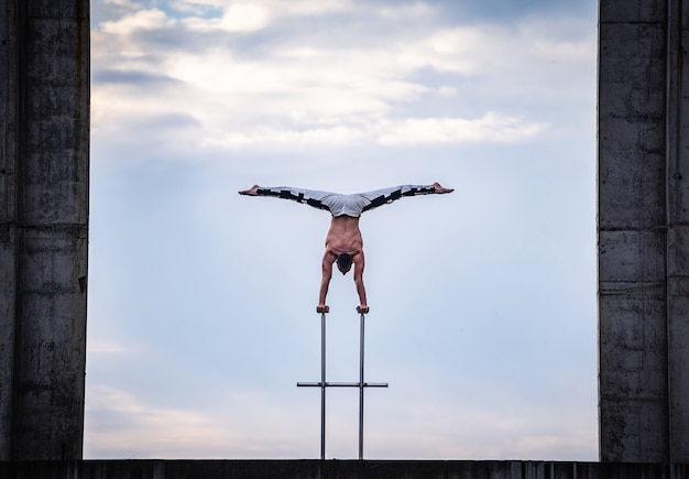 Artiste de cirque masculin flexible faisant le poirier contre un paysage nuageux incroyable et des constructions modernes. Concept de symétrie, d'équilibre et de créativité.