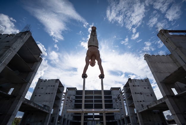 Artiste de cirque masculin flexible faisant le poirier contre un paysage nuageux incroyable et des constructions modernes. Concept de symétrie, d'équilibre et de créativité.