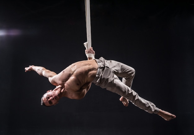 Artiste de cirque sur les sangles aériennes avec des muscles forts sur fond noir