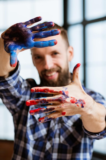 Artiste délice inspiration imagination peintre souriant regardant la caméra cadre mains avec de la peinture bleu rouge sur Say cheese