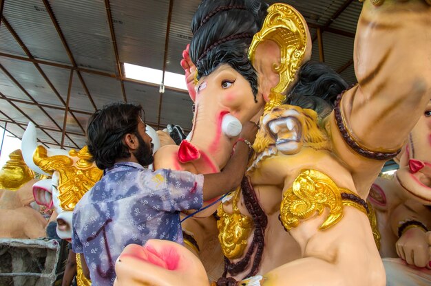 Artiste faisant une statue et donne la touche finale à une idole du dieu hindou Lord Ganesha lors d'un atelier d'artiste pour le festival Ganesha