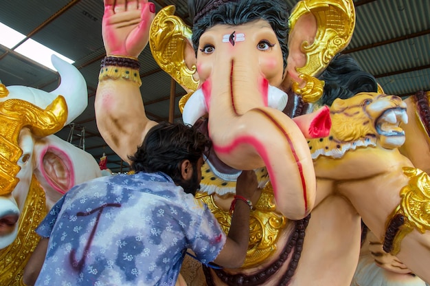 Artiste faisant une statue et donne la touche finale à une idole du dieu hindou Lord Ganesha lors d'un atelier d'artiste pour le festival Ganesha