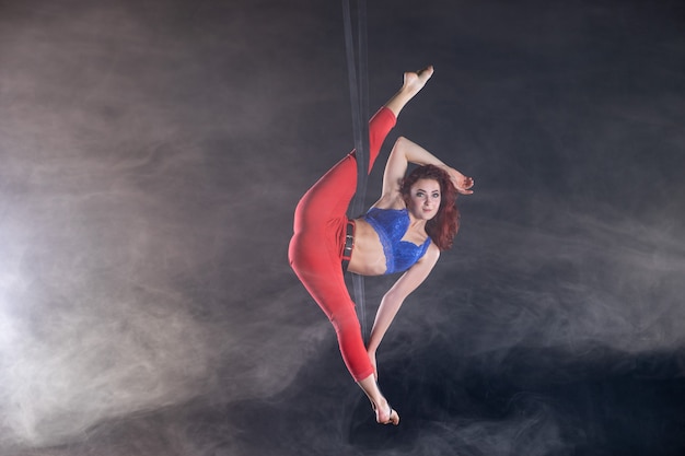 Artiste féminine de cirque aérien athlétique, sexy et flexible avec rousse sur des sangles aériennes sur fond noir.