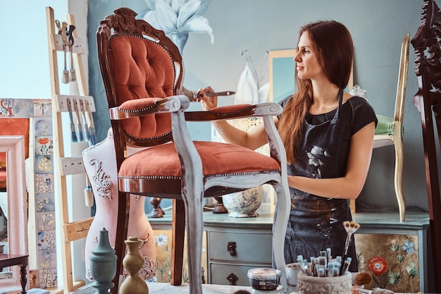 Artiste féminine en tablier peinture chaise vintage de couleur blanche avec pinceau en atelier.